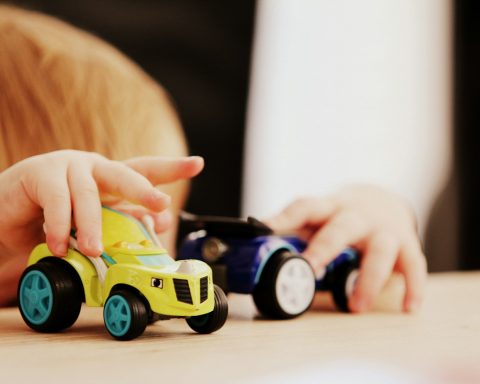 child playing with two assorted-color car plastic toys on brown wooden table